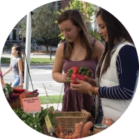 A photo of two women picking out fresh produce from the MSU Student Organic Farm Stand outside of the MSU Auditorium.